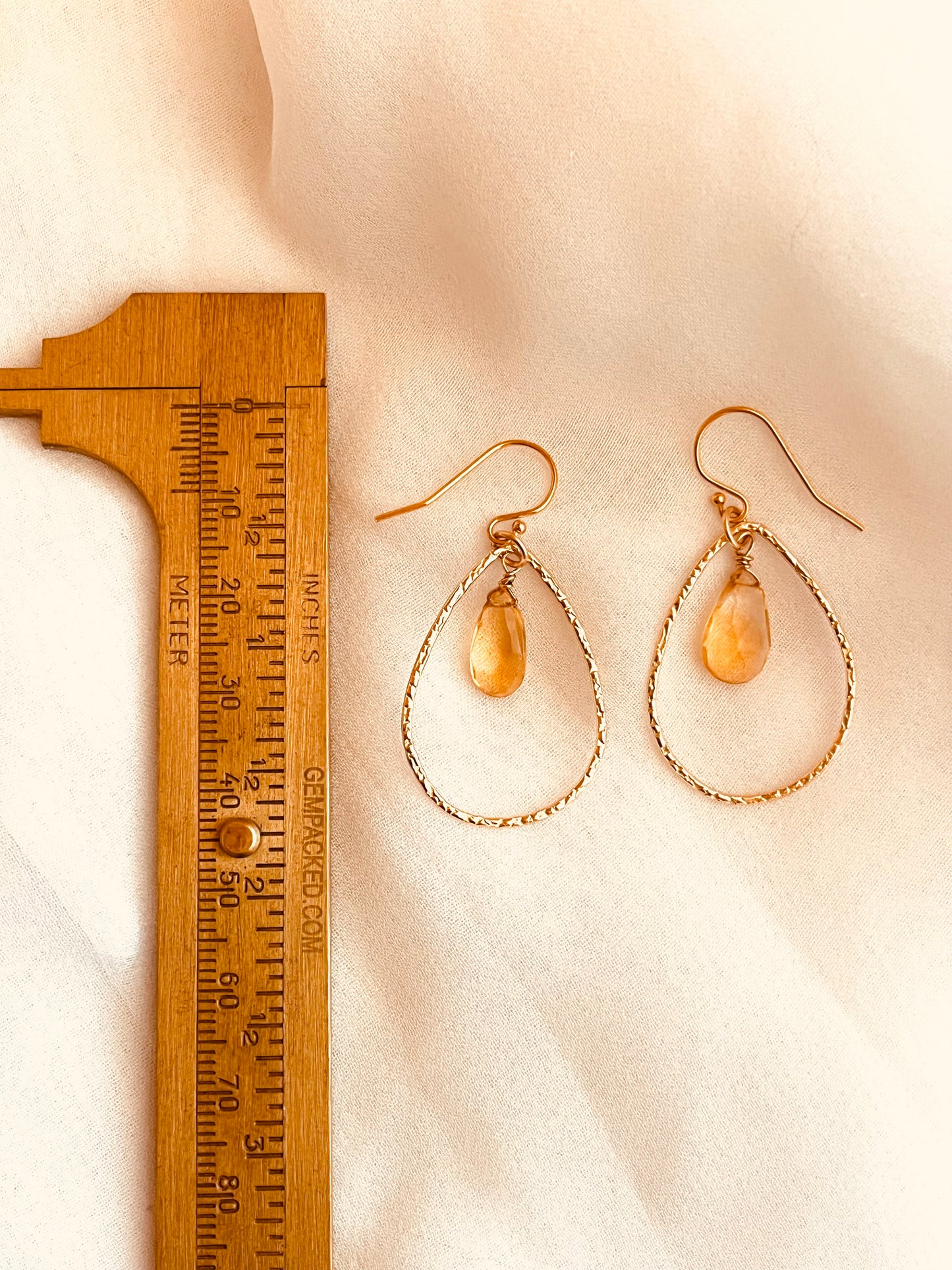 Elegant and lightweight, these handcrafted earrings feature warm yellow teardrop gemstones suspended inside textured 14k gold-filled teardrop hoops. Each stone catches the light with a soft shimmer, adding a refined pop of color to any outfit. The delicate hammered finish on the hoops adds subtle detail and dimension, perfect for both everyday wear and special occasions. Made with care and precision, these earrings combine timeless design with artisan craftsmanship.
