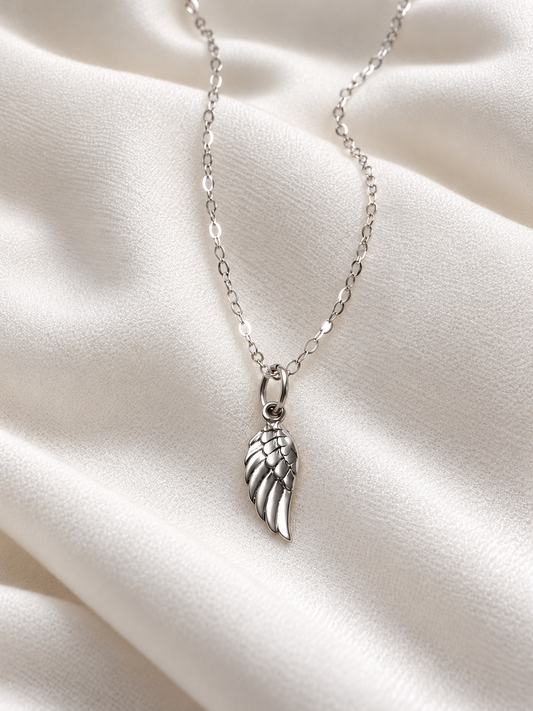 sterling Silver Dainty silver angel wing necklace with delicate feather pendant on soft ivory fabric