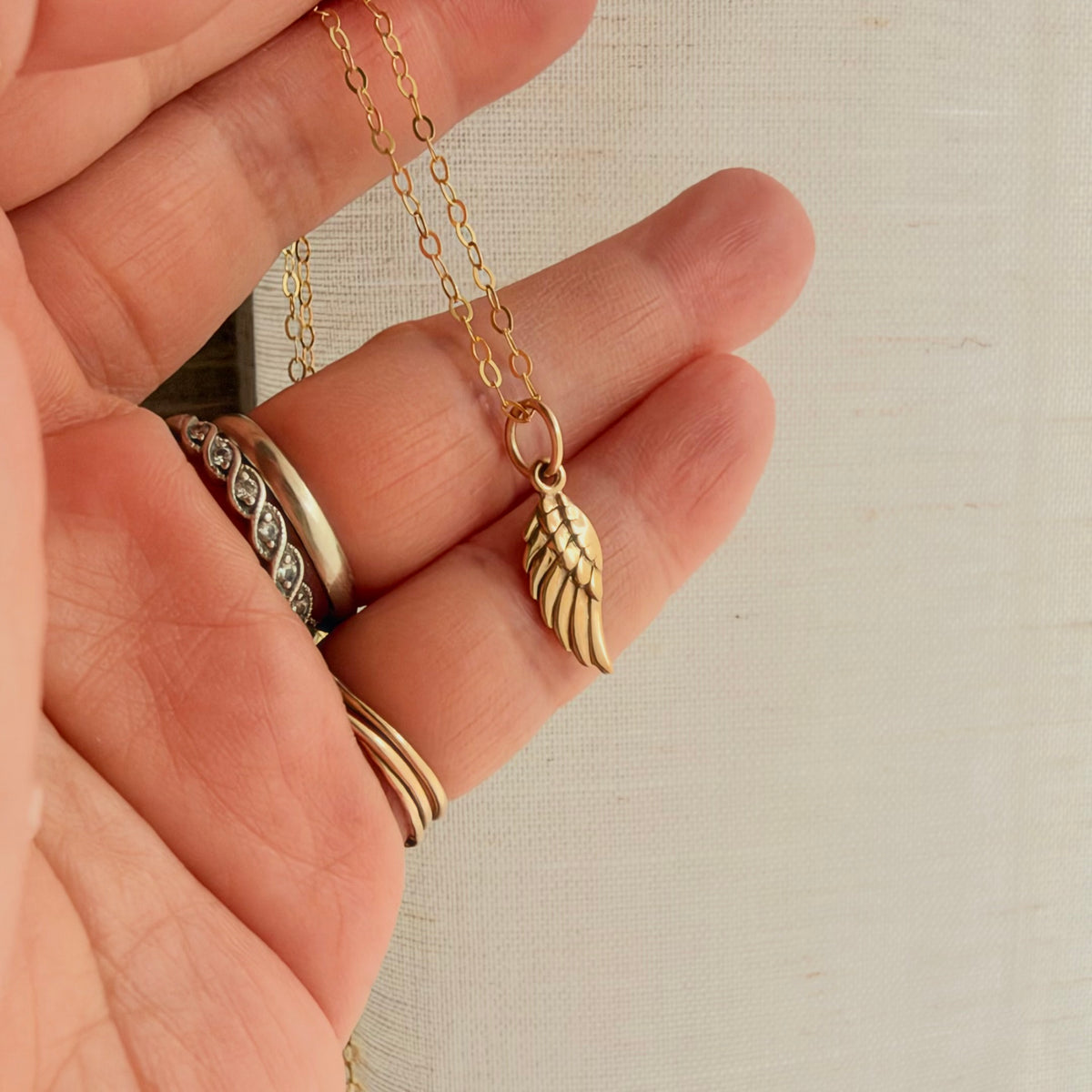 Tiny bronze angel wing pendant on 14K gold filled chain, showing its delicate 16mm size