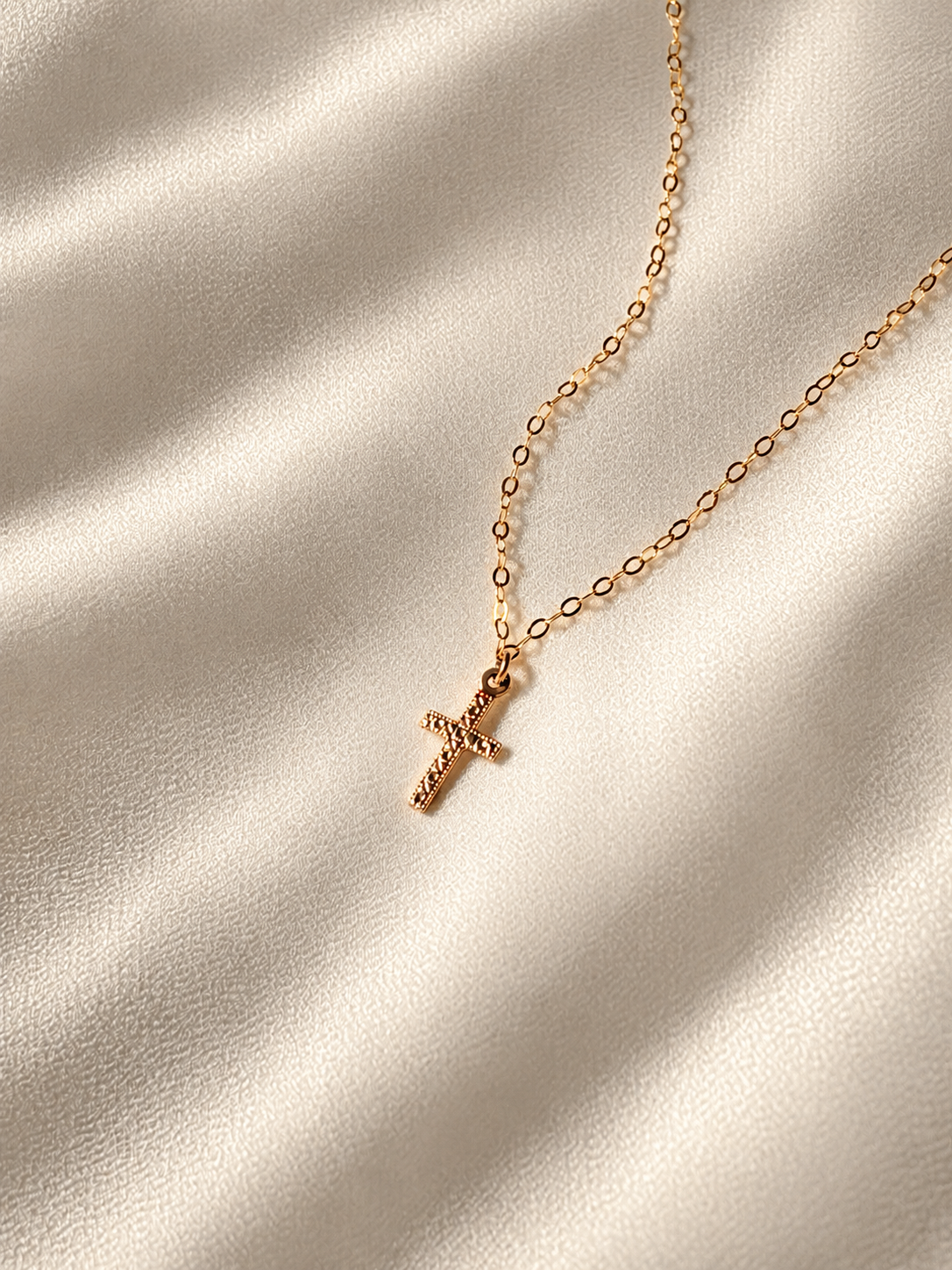 Minimalist 14K gold filled cross necklace with a delicate oval link chain and small double-sided religious cross charm on a neutral fabric background.