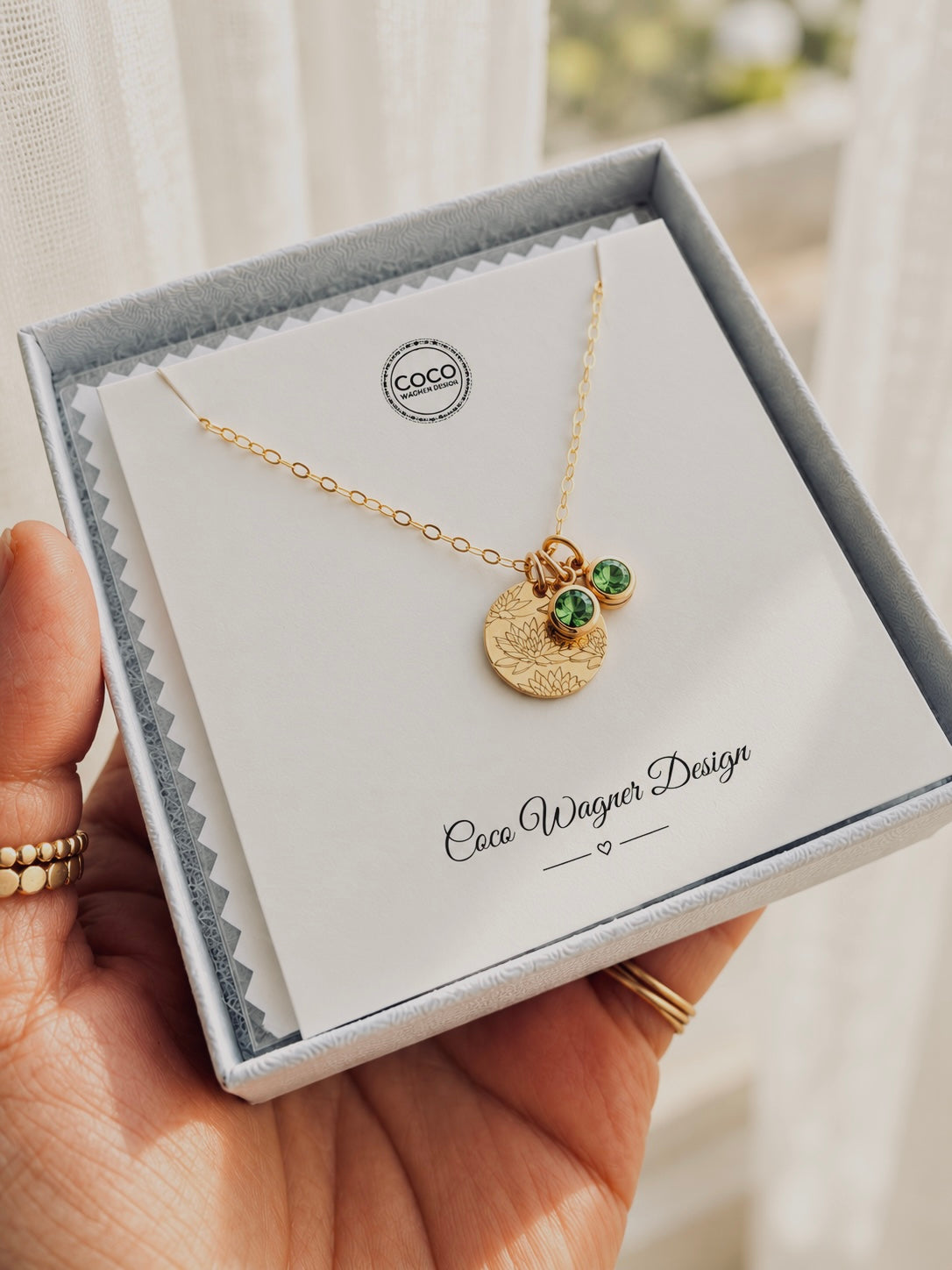 Personalized gold birth flower disc necklace with two green birthstone charms, displayed in Coco Wagner Design gift packaging, handmade in Wyoming.