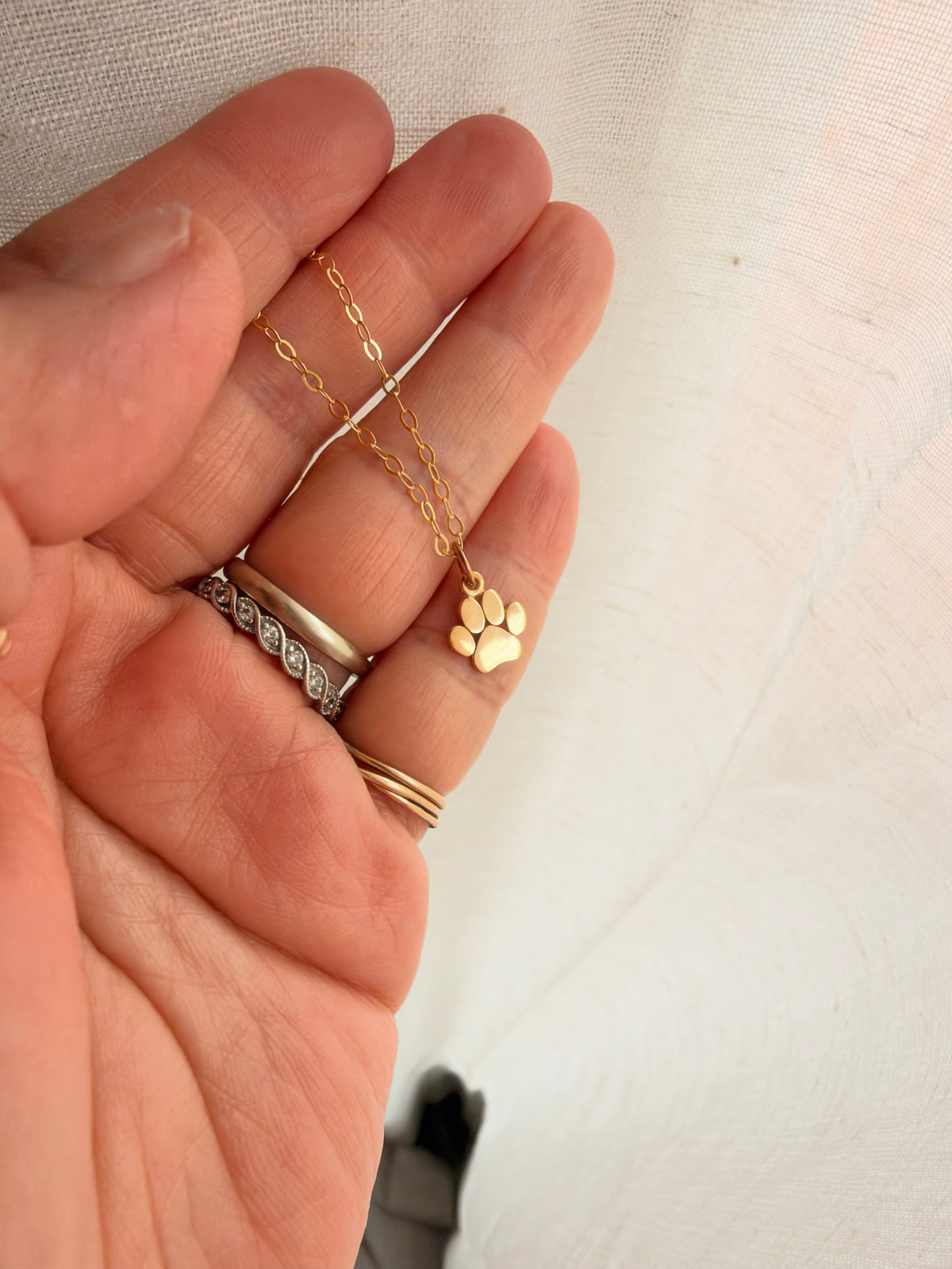 Gold paw print charm necklace with delicate 14K gold filled chain, shown in hand for size reference.