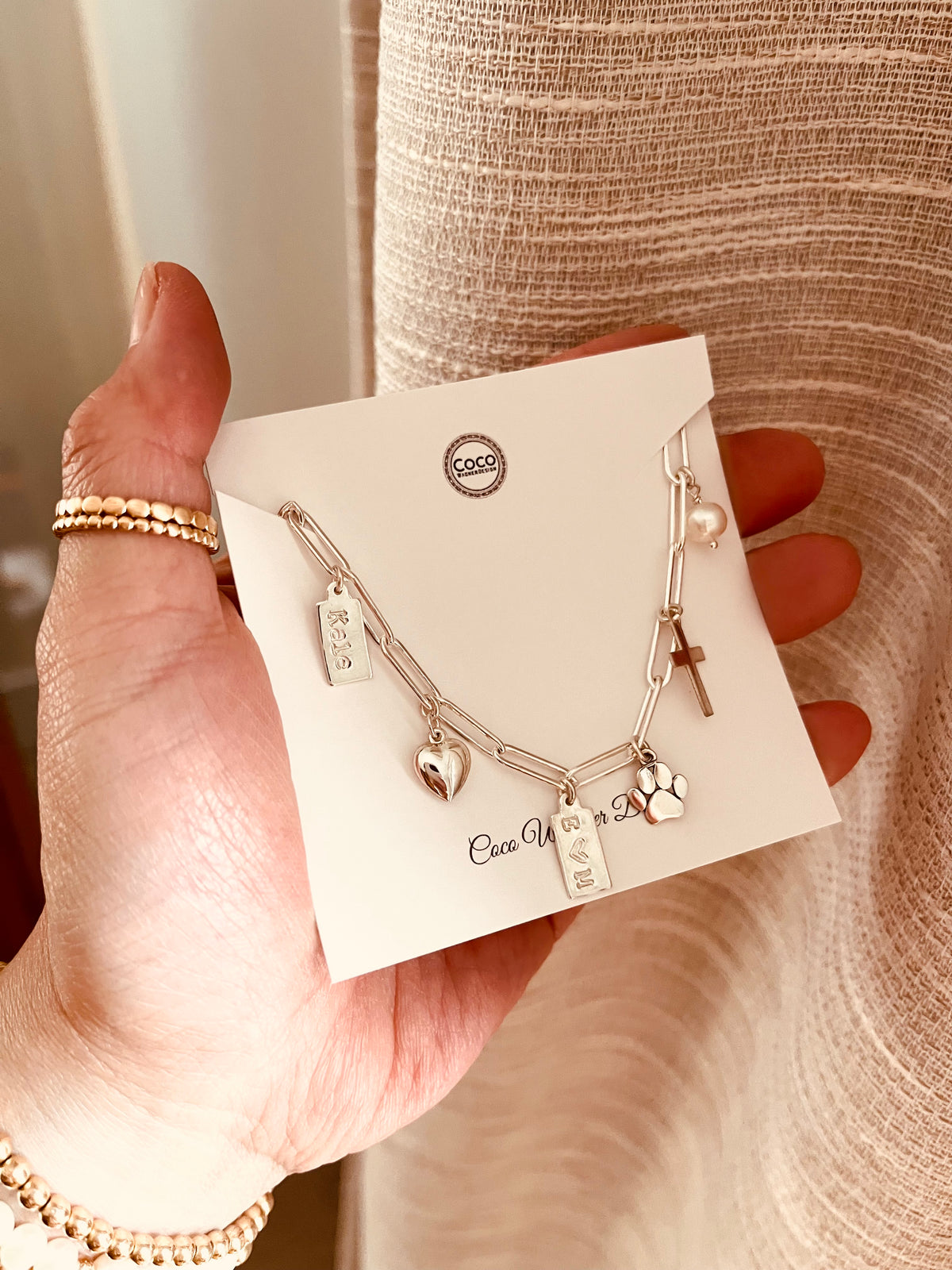 Personalized sterling silver charm bracelet worn on wrist with heart initial tag and paw print charm